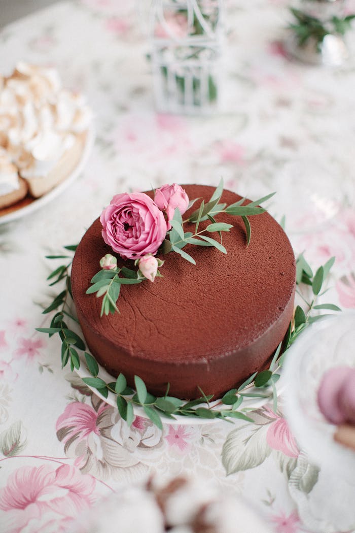 Elegant chocolate cake adorned with pink roses and leaves, perfect for celebrations.